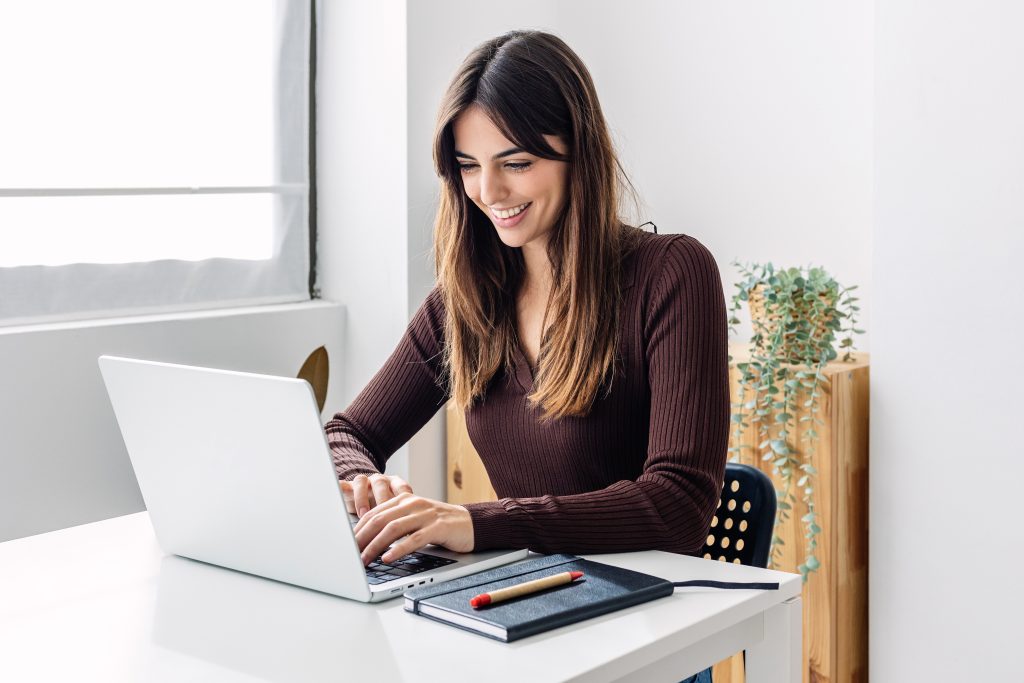 Confident young adult businesswoman working on laptop computer at home office